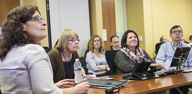 Photo of a group of professionals sitting at a table viewing a presentation.  