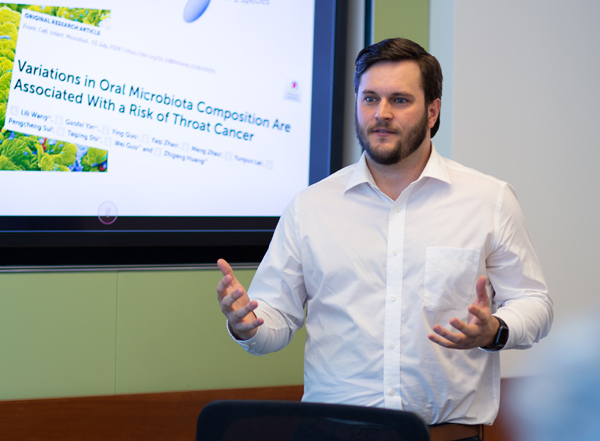 A male professional giving a presentation next to a visual portraying the text Variations in oral microbiota composition are associated with a risk of throat cancer.